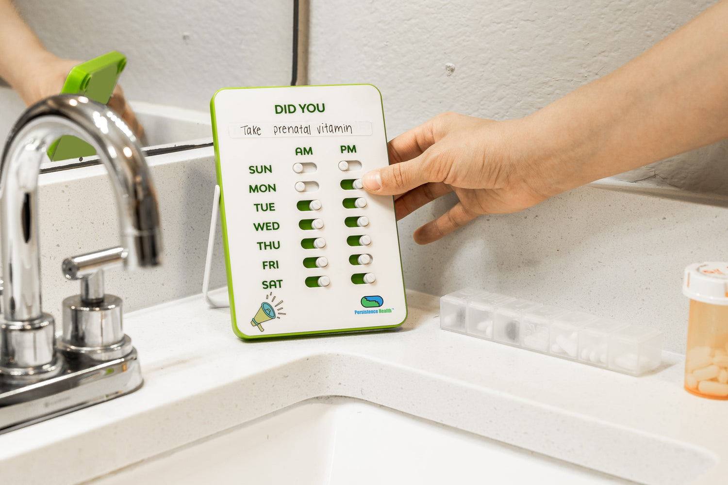 Hand holding a weekly pill organizer next to a sink