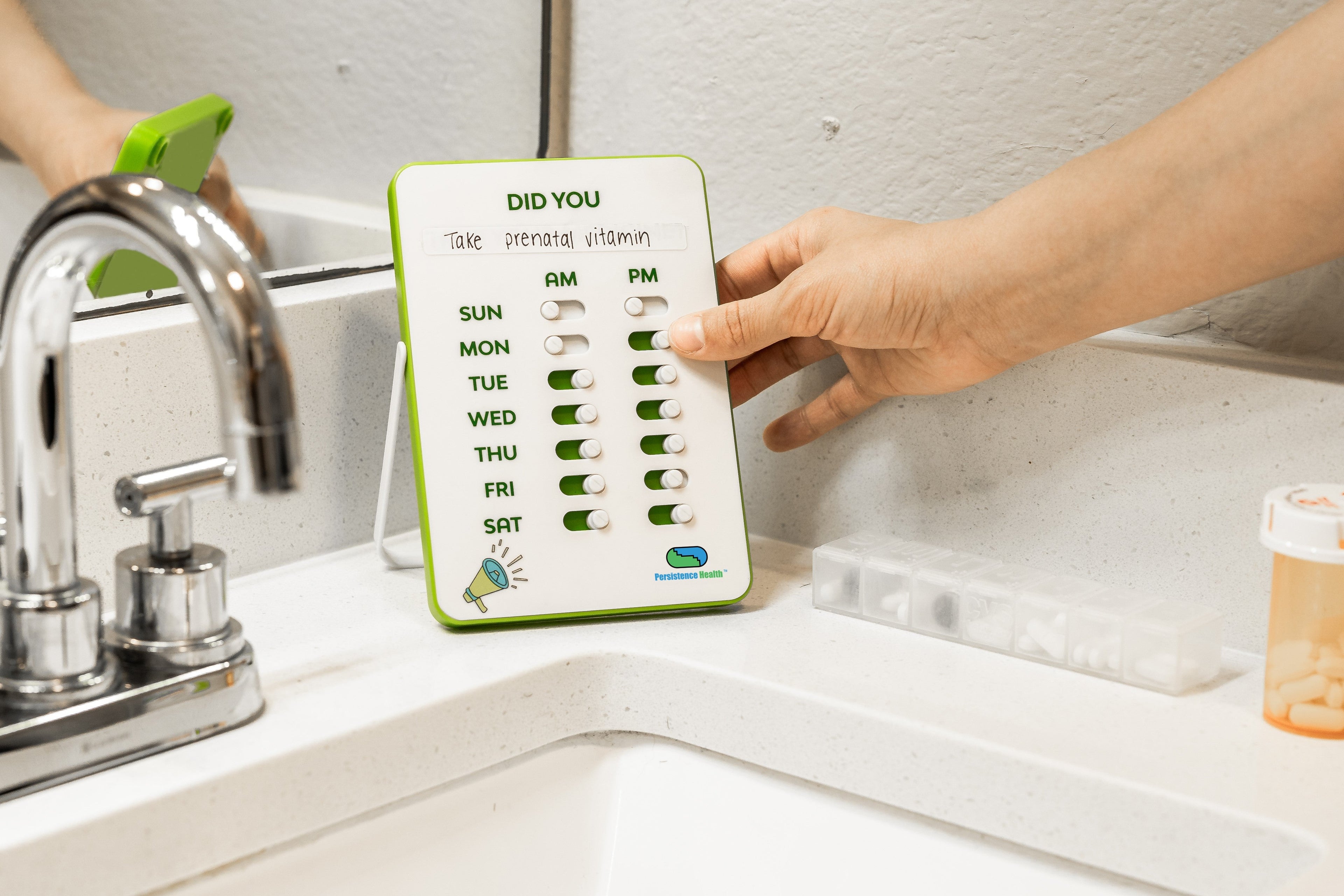 Hand holding a weekly pill organizer next to a sink