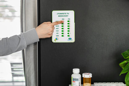 Person pointing at a medication reminder chart on a refrigerator door with bottles below.