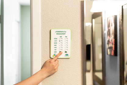 Hand pressing a digital pill reminder on a refrigerator door.