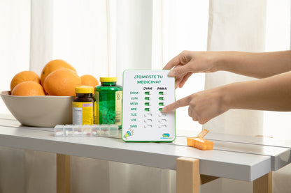 Person using a digital pill organizer on a table with fruits and bottles in the background